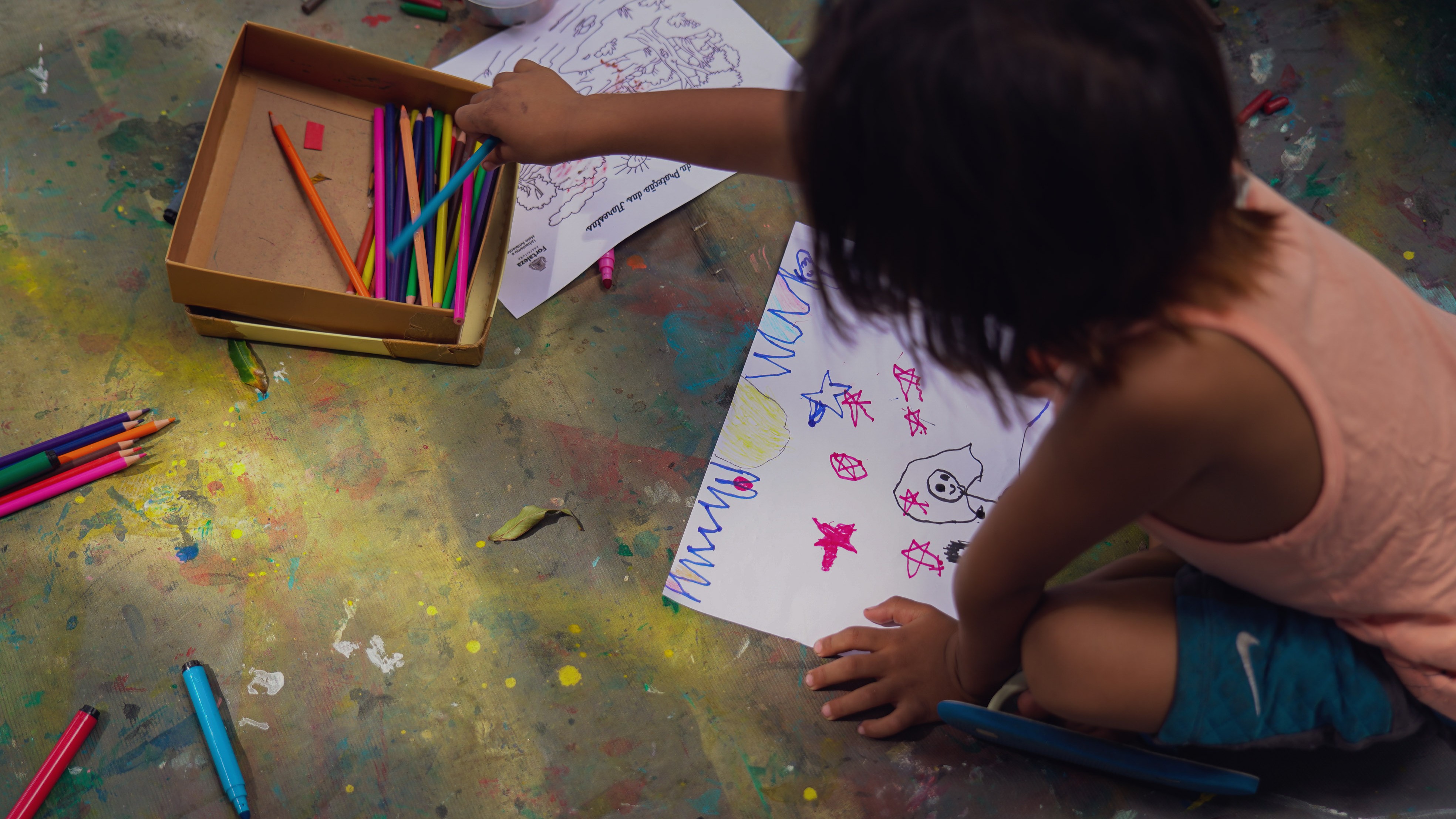 uma criança desenhando num papel branco com lápis de cera